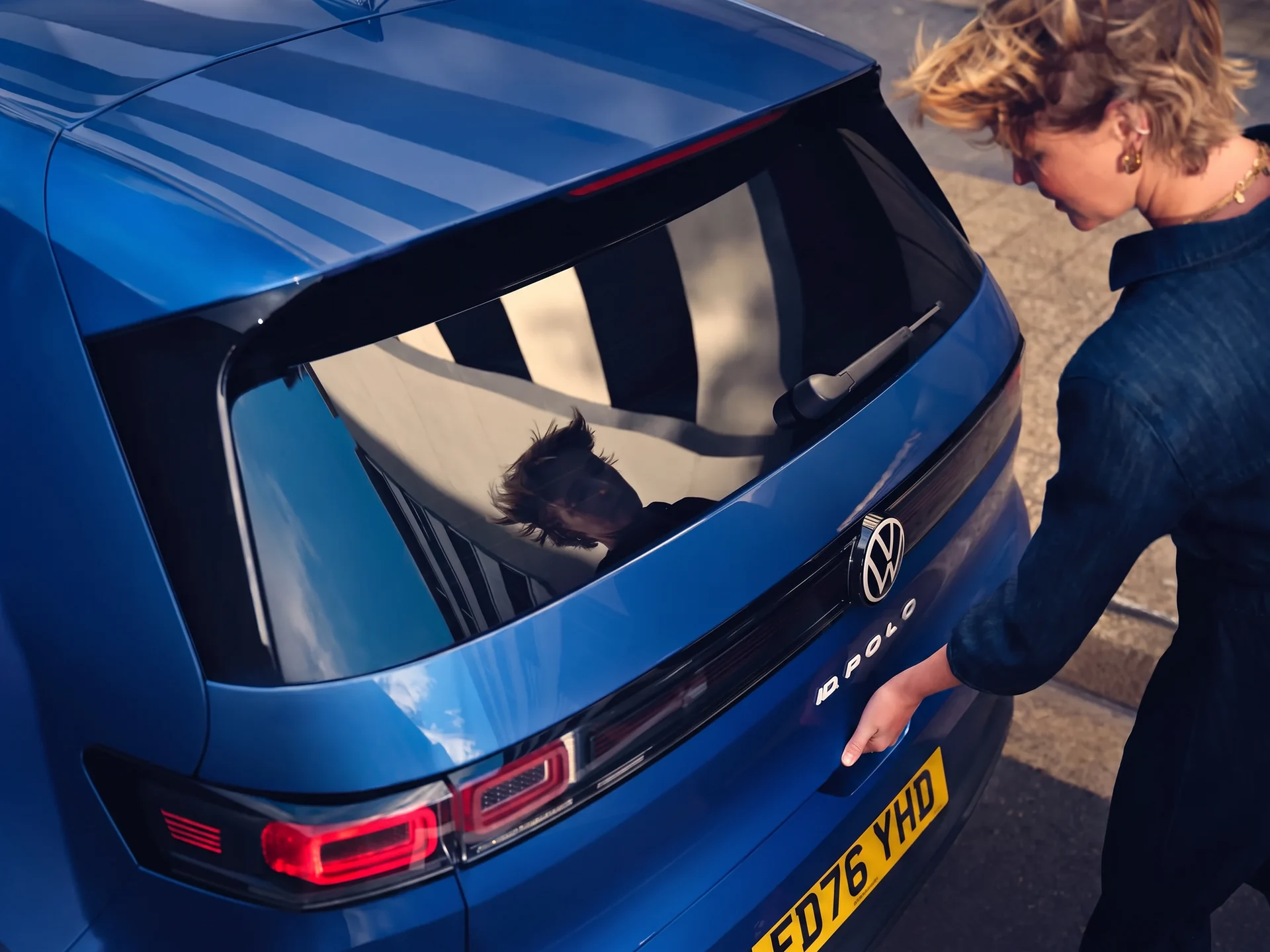 Woman opening the tailgate of a blue Volkswagen ID. Polo, showing the rear badging