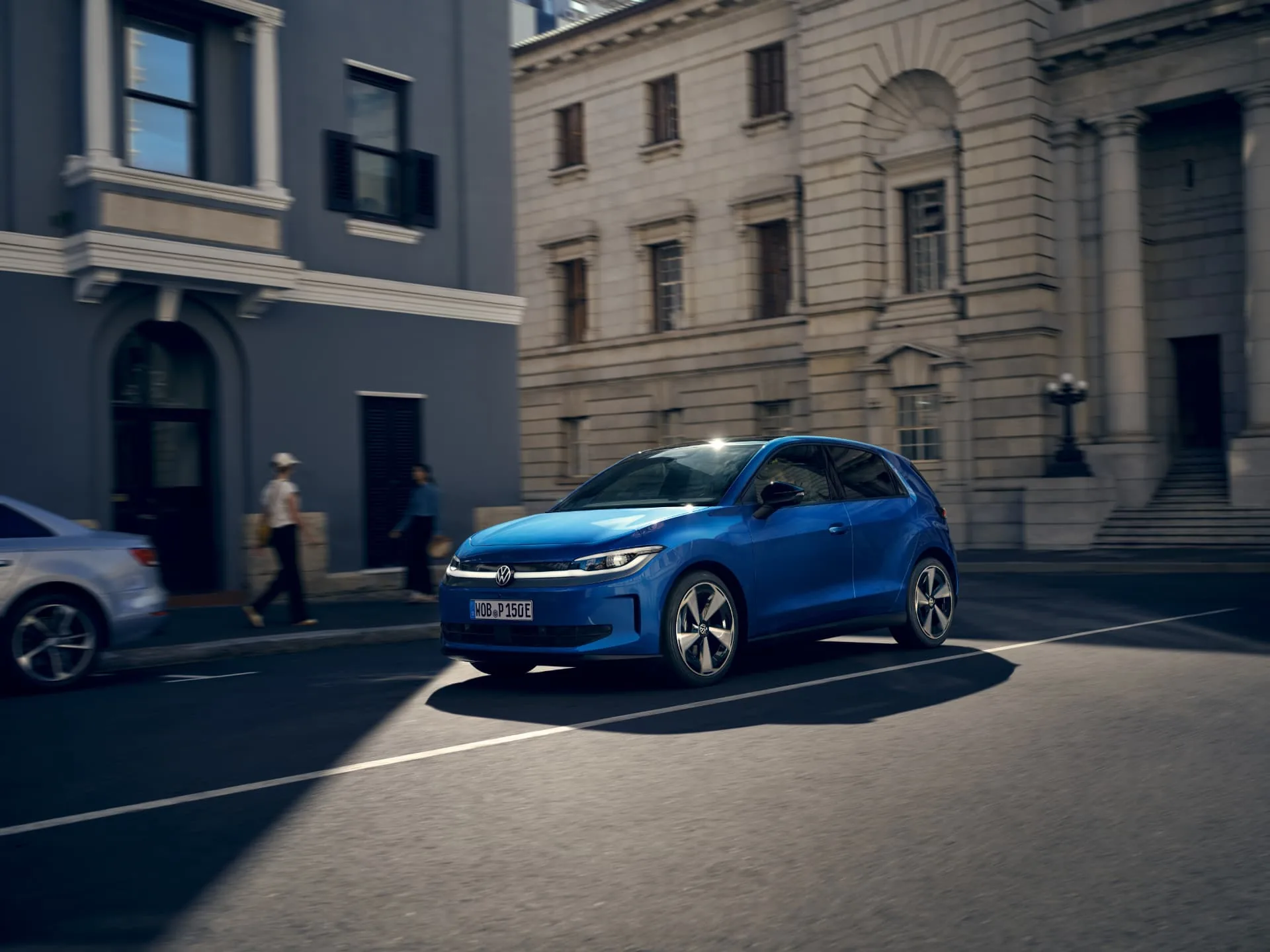 Blue Volkswagen ID. Polo driving through a city street past classical stone buildings