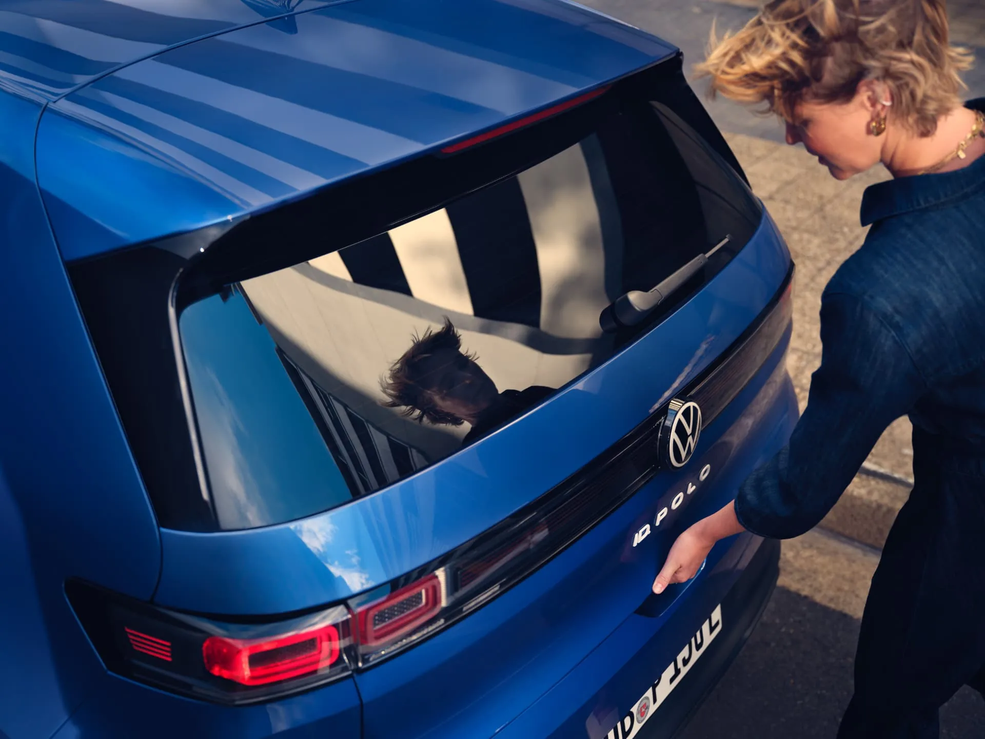 Woman opening the tailgate of a blue Volkswagen ID. Polo, showing the rear badging